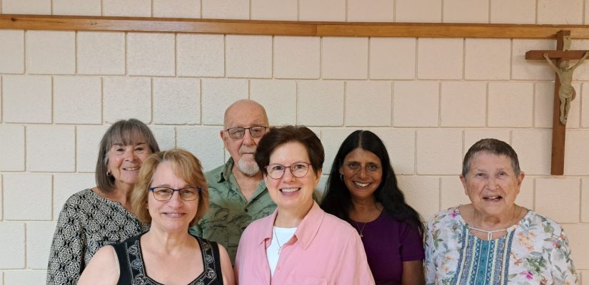 6 individuals stand in front of a wall with a crucifix