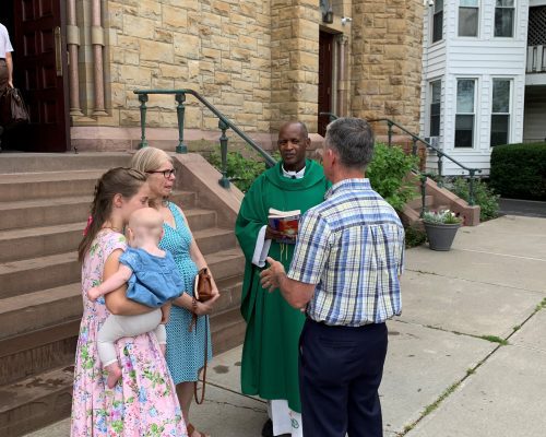 people stand outside a church talking to Priest