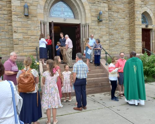 people gather on steps after Mass talking with Priest