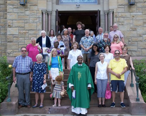 People gather on the steps of a church with the Priest.
