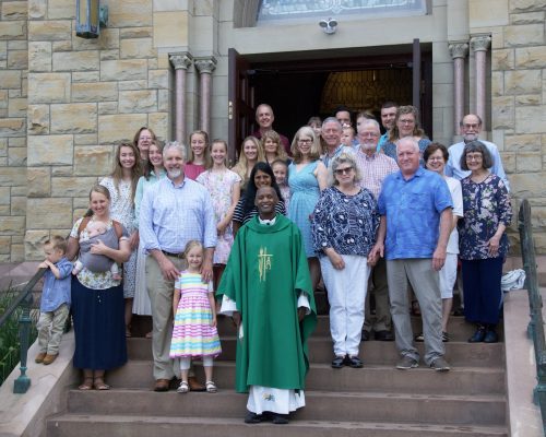 People stand on the steps of a church with a Priest.