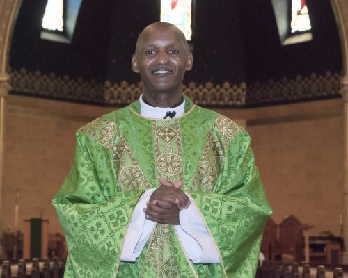 A vested Priest stands inside a church.