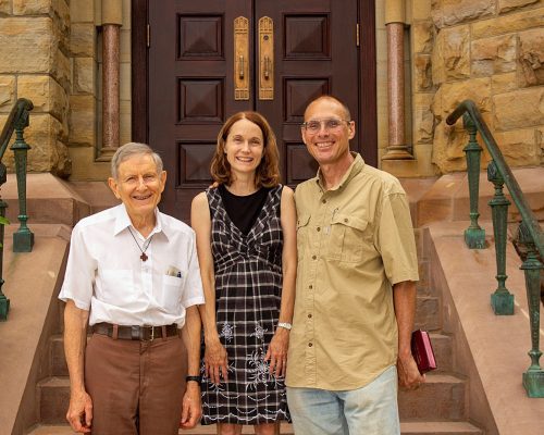 Two men and a woman stand at the bottom of the church steps
