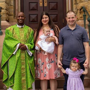 A Priest stands with a couple holding a baby.