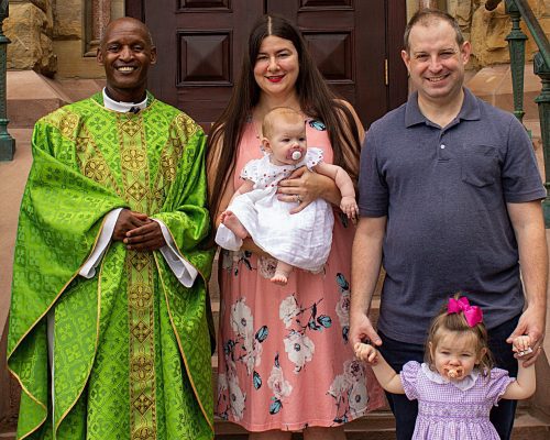 A Priest stands with a couple holding a baby.