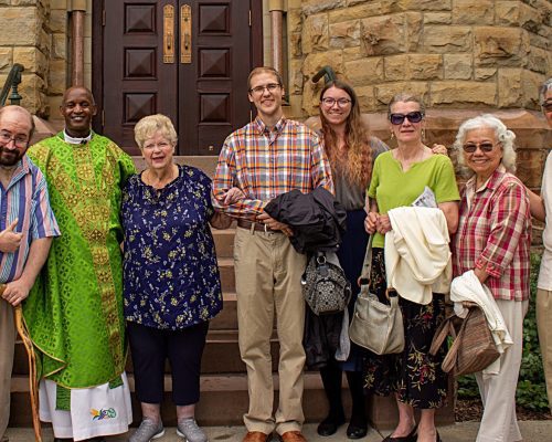 several people stand around a priest at the bottom of the church steps