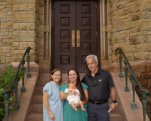 An older man and woman stand beside a younger woman holding a baby