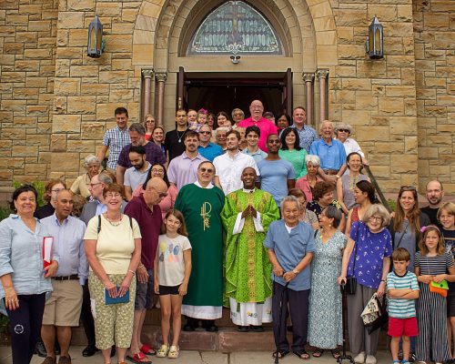 A large group of people stand outside the church on the steps