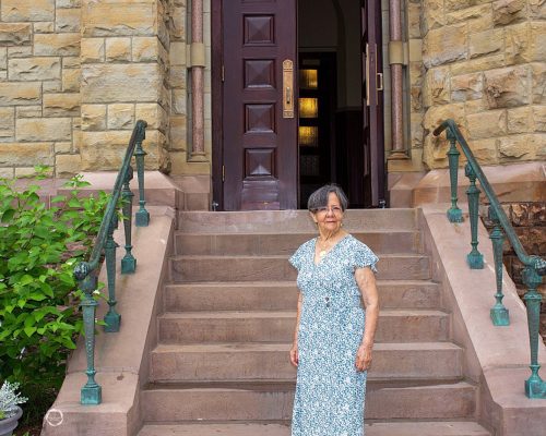 A woman stands at the bottom of the steps to the church.