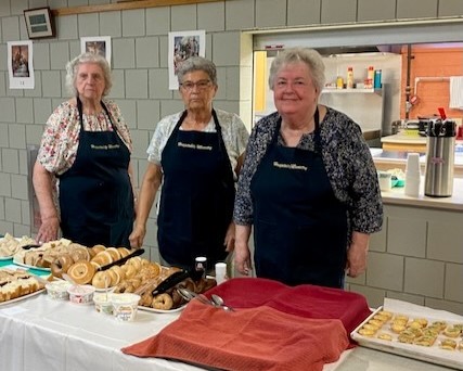 3 women stand with treats on a table