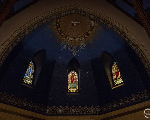 Sanctuary architecture with stained glass windows of Jesus, Mary, and Joseph and light illuminating the painted dove.