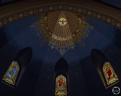 Sanctuary architecture with stained glass windows of Jesus, Mary, and Joseph and light illuminating the painted dove.