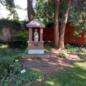 Virgin Mary statue surrounded by brick and stone with Ave Maria Gratia Plena marker among a garden