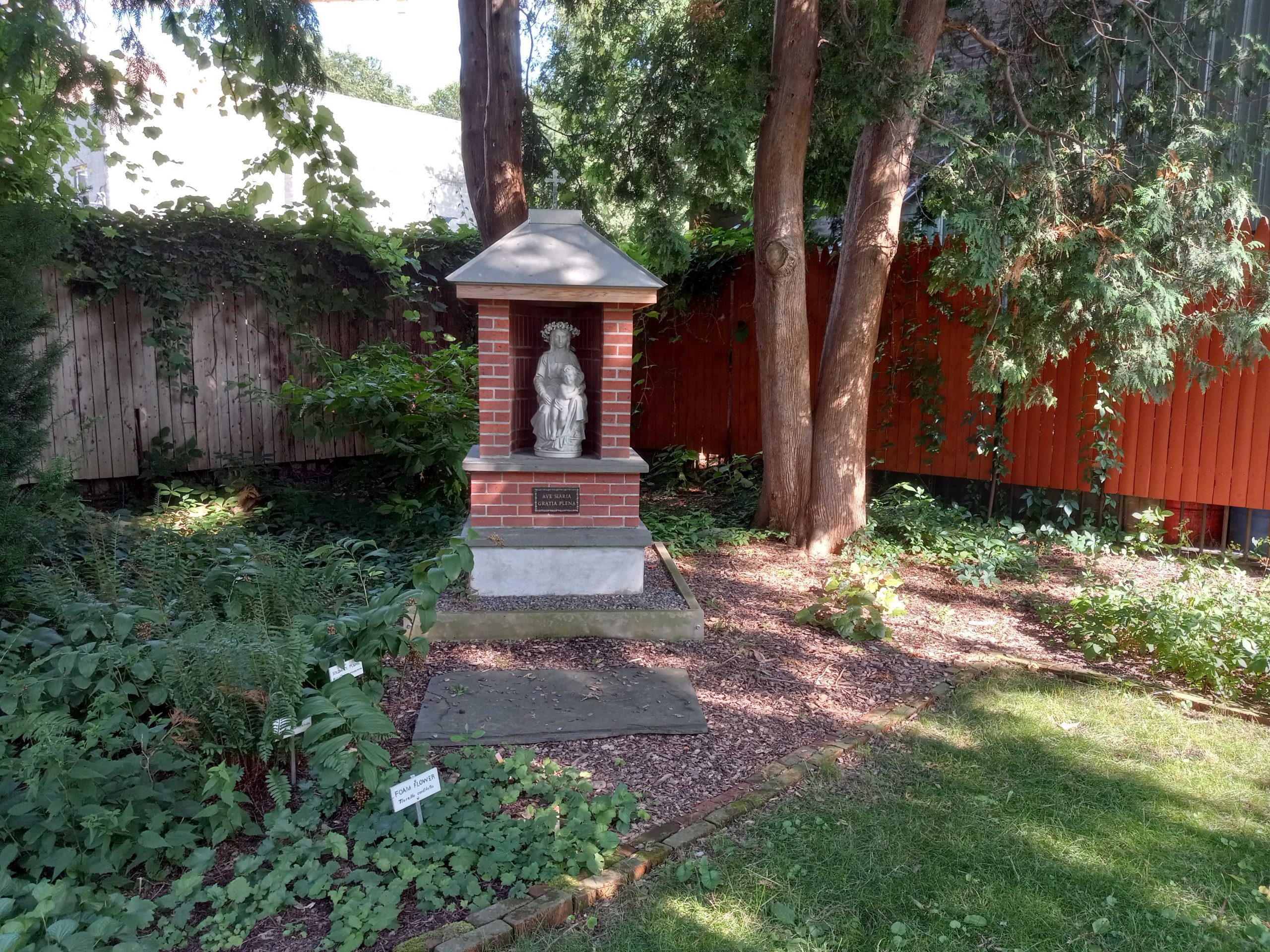 Virgin Mary statue surrounded by brick and stone with Ave Maria Gratia Plena marker among a garden