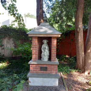 Virgin Mary statue surrounded by brick and stone with Ave Maria Gratia Plena marker among a garden.
