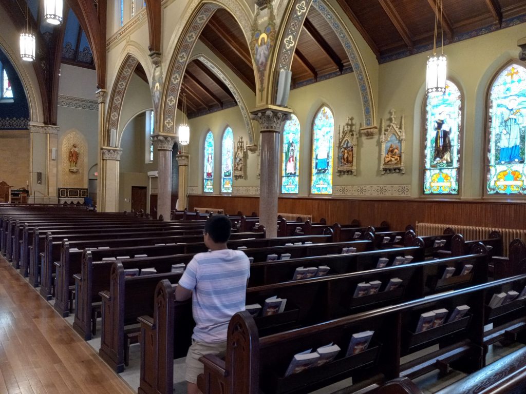 a young man kneels and prays in church