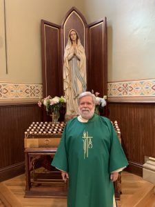 Deacon standing in front of Blessed Mother statue with votive candles
