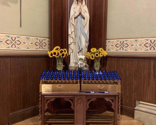 A statue of the Blessed Mother with lit candles and flowers