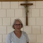 A smiling woman is standing in front of a crucifix