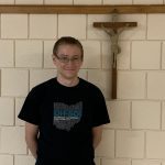 A smiling man is standing in front of a crucifix