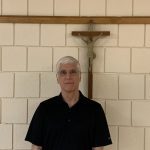 A man is standing in front of a crucifix