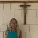 A smiling woman is standing in front of a crucifix