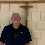 A smiling man is standing in front of a crucifix