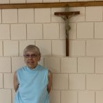 A smiling woman is standing in front of a crucifix