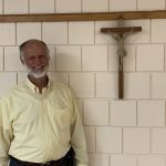 A smiling man standing in front of a crucifix