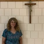 A smiling woman standing in front of a crucifix