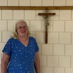 A woman in blue is standing in front of a crucifix