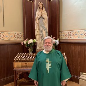 Deacon standing in front of Blessed Mother statue with votive candles