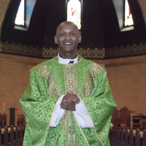 A vested Priest stands inside a church.